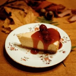 Close-up of a cheesecake slice topped with cherry sauce on a floral plate, ideal for food photography.